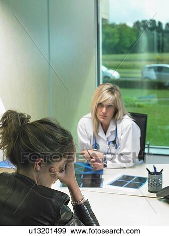 Concerned female doctor at her desk with stressed patient in foreground. X rays on desk. View Large Photo Image Stock Photo - Concerned female doctor at her desk with stressed patient in foreground. X rays on desk.. Fotosearch
