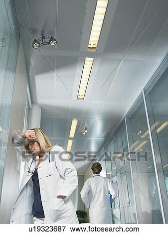 Concerned female doctor in lobby of a hospital another female doctor walking away. View Large Photo Image Stock Photo - Concerned female doctor in lobby of a hospital another female doctor walking away.. Fotosearch