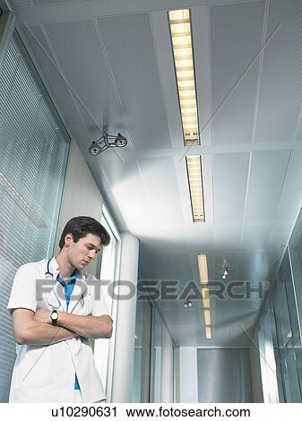 Stock Image - Concerned young doctor in a lobby of a hospital. Low angle.. Fotosearch