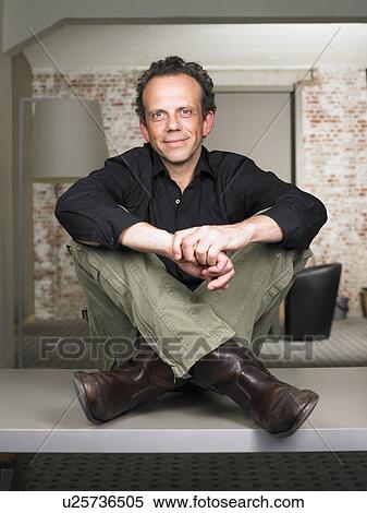 Smiling businessman sitting on desk. Brussels, Belgium. View Large Photo Image Stock Photography - Smiling businessman sitting on desk. Brussels, Belgium.. Fotosearch