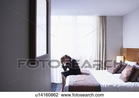 Stock Image - Woman sitting on edge of bed with head in hands. Fotosearch