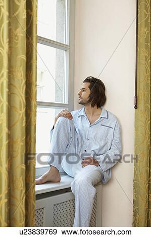 young man sitting on window sill wearing pyjamas looking out of window View Large Photo Image Stock Photo - young man sitting on window sill wearing pyjamas looking out of window. Fotosearch