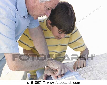 Stock Photo - Boy (8-10) and grandfather leaning on car bonnet, looking at road map. Fotosearch