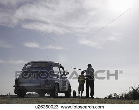 Stock Image - Boy (8-10) and grandfather standing beside car, senior man pointing with cane. Fotosearch