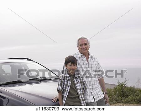 Stock Photo - Boy (8-10) and grandfather standing beside car at beach, smiling, portrait. Fotosearch