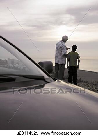 Stock Photography - Boy (8-10) and grandfather standing near car at beach, talking, rear view. Fotosearch