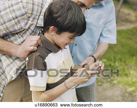 Stock Image - Boy (8-10) looking at digital camera with father and grandfather, side view. Fotosearch