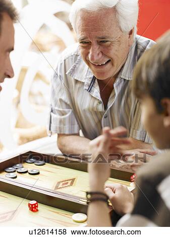 Stock Photo - Boy (8-10) playing backgammon with father and grandfather (differential focus). Fotosearch