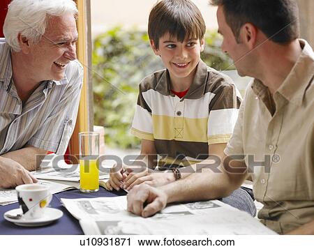 Stock Image - Boy (8-10) sitting in café with father and grandfather, smiling. Fotosearch