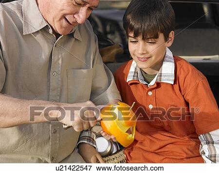 Stock Photo - Boy (8-10) watching grandfather peel orange with knife, smiling, close-up. Fotosearch