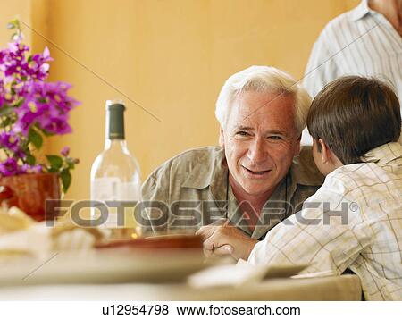 Boy (8-10) whispering in grandfather's ear at dining table View Large Photo Image Stock Photo - Boy (8-10) whispering in grandfather's ear at dining table. Fotosearch