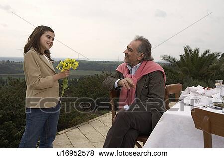 Girl (9-11) giving flowers to grandfather at a table outside View Large Photo Image Stock Photo - Girl (9-11) giving flowers to grandfather at a table outside. Fotosearch