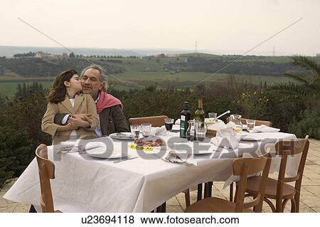 Stock Photo - Girl (9-11) kissing her grandfather at a table outside. Fotosearch