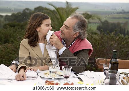 Girl (9-11) sitting with grandfather at a table outside View Large Photo Image Stock Photo - Girl (9-11) sitting with grandfather at a table outside. Fotosearch