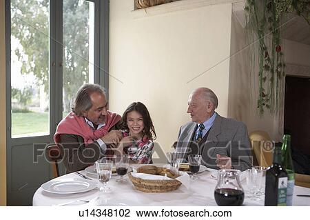 Stock Image - Great grandfather watching grandfather and granddaughter (5-7) at dinner table. Fotosearch