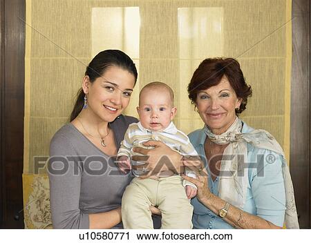 Stock Image - Mother and grandmother holding baby boy (1-3 months) smiling, portrait. Fotosearch