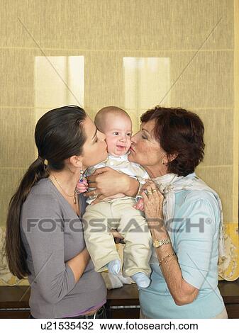Stock Image - Mother and grandmother kissing baby boy (1-3 months). Fotosearch