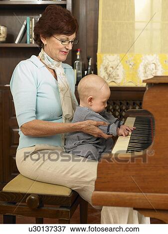 Stock Photo - Senior grandmother playing piano with baby grandson (1-3 months). Fotosearch