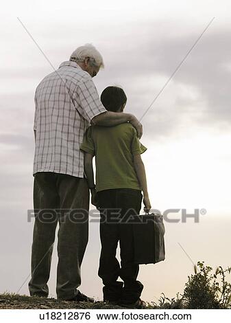 Stock Photograph - Senior man standing with arm around grandson (8-10), boy carrying case. Fotosearch