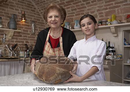 Stock Photo - Senior woman and granddaughter (9-11) holding loaf, portrait. Fotosearch
