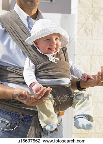 Stock Image - Close up of baby (5 months) in sling on father's chest, Alicante, Spain,. Fotosearch