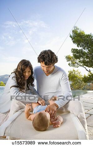 Couple changing a baby's diaper by an infinity pool. View Large Photo Image Stock Photo - Couple changing a baby's diaper by an infinity pool.. Fotosearch