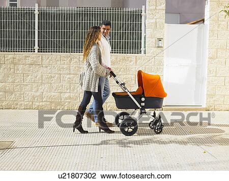 Stock Image - Couple walking with pram on pavement, Alicante, Spain,. Fotosearch