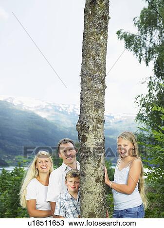Stock Image - Family outdoors by tall tree smiling.. Fotosearch