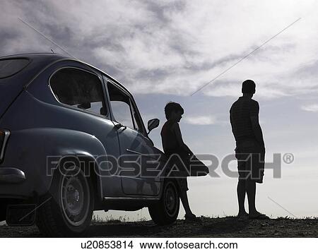 Picture - Father and son (8-10) standing beside parked car, looking at view (backlit). Fotosearch