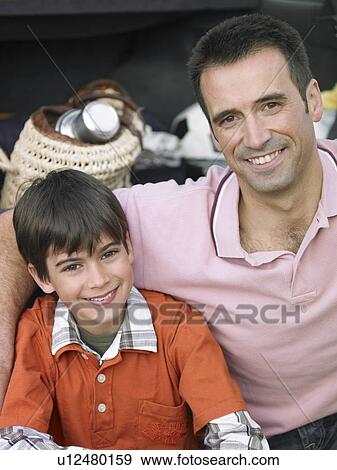 Stock Photo - Father sitting with arm around son (8-10), smiling, portrait. Fotosearch