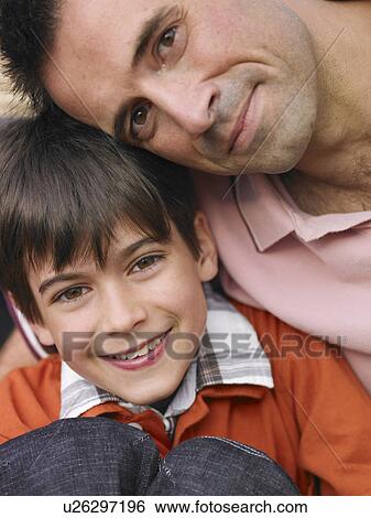 Stock Photograph - Father sitting with arm around son (8-10), smiling, close-up, portrait. Fotosearch