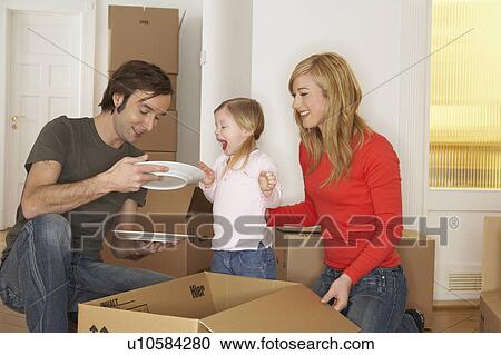 Stock Image - Girl (3-5) with parents unpacking cardboard boxes, smiling. Fotosearch