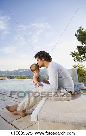 Stock Photography - Man kissing a baby by an infinity pool.. Fotosearch