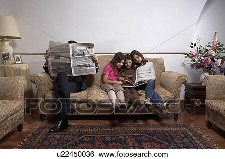Stock Photograph - Man reading newspaper on sofa with daughters(5-11). Fotosearch