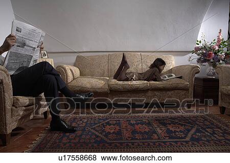 Man reading newspaper with daughter (5-7) reading book on sofa View Large Photo Image Stock Photo - Man reading newspaper with daughter (5-7) reading book on sofa. Fotosearch