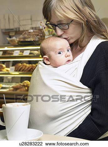 Stock Image - Mother kissing baby son (1-3 months) on head in cafe. Fotosearch