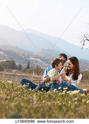 Parents and son (6-8) sitting in field, holding flowers, smiling View Large Photo Image Stock Photograph - Parents and son (6-8) sitting in field, holding flowers, smiling. Fotosearch