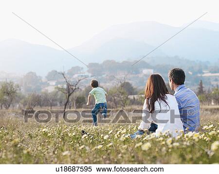 Parents sitting in field watching son (6-8) running View Large Photo Image Stock Photography - Parents sitting in field watching son (6-8) running. Fotosearch