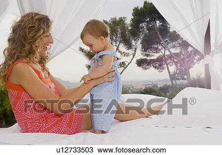 Stock Image - Woman and baby on bed outdoors.. Fotosearch