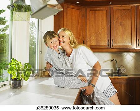 Stock Photography - Woman and young boy embracing in kitchen smiling.. Fotosearch