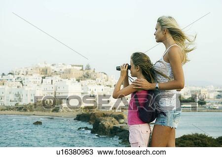 Stock Image - Woman and young girl with binoculars looking over the water in Greece.. Fotosearch