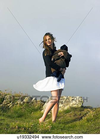 Picture - Young woman holding baby with the wind blowing her skirt.. Fotosearch