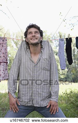 Stock Image - Man hanging on clothesline with clothespins smiling.. Fotosearch