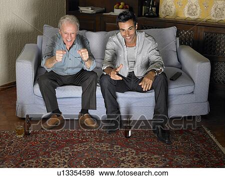 Senior man and younger man watching television on sofa. Alicante, Spain. View Large Photo Image Stock Photo - Senior man and younger man watching television on sofa. Alicante, Spain.. Fotosearch