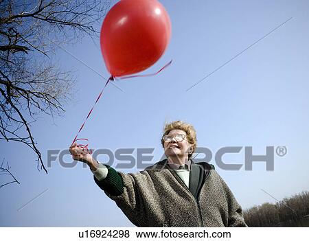 Senior woman outdoors holding red balloon, smiling, low angle view View Large Photo Image Stock Photo - Senior woman outdoors holding red balloon, smiling, low angle view. Fotosearch