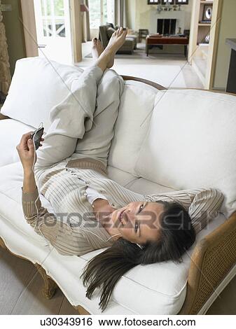 Woman listening to MP3 Player on sofa indoors smiling. View Large Photo Image Stock Photograph - Woman listening to MP3 Player on sofa indoors smiling.. Fotosearch