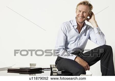 Stock Image - Young businessman seated on desk.. Fotosearch