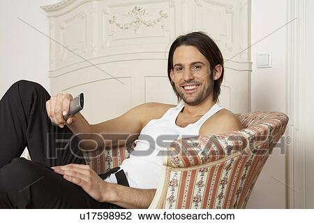 Stock Image - young man holding remote control smiling, portrait. Fotosearch