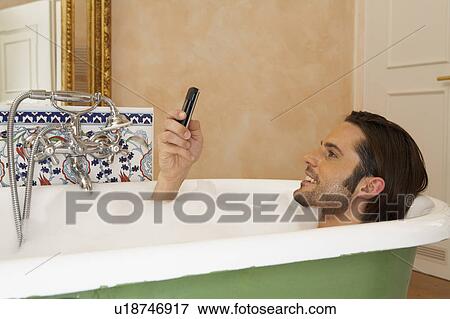 young man smiling holding mobile phone in bath, high section, profile View Large Photo Image Stock Photo - young man smiling holding mobile phone in bath, high section, profile. Fotosearch