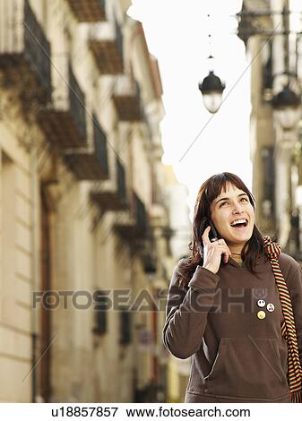 Stock Photo - Young woman using mobile phone in street, smiling. Fotosearch